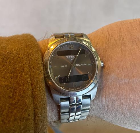 Titanium coloured Tissot wristwatch, peaking from behind a mid brown wool jacket