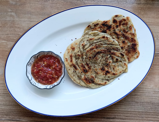Das fertige Gericht auf dem Teller. 2 Fladen und ein Schälchen der geraspelten Tomate 

In den fertig gebratenen Fladen sieht man deutlich die Streifenstruktur