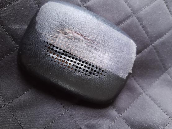 Photo of the square Bowers and Wilkins swishy headphone pad, with some medical tape covering a tear in the black perforated fabric earhole part.