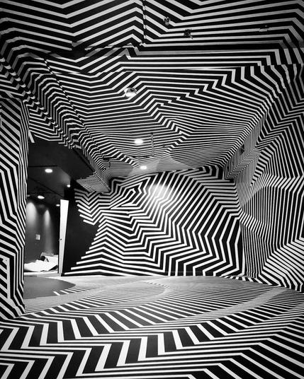 A black room covered in white tape lines creating jagged and curving indentations across the walls and floor.