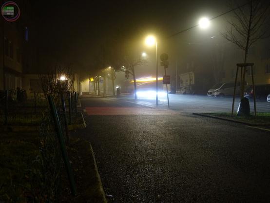 Städtische Straße nachts im Nebel, ein Bus mit Bewegungsunschärfe rauscht durch