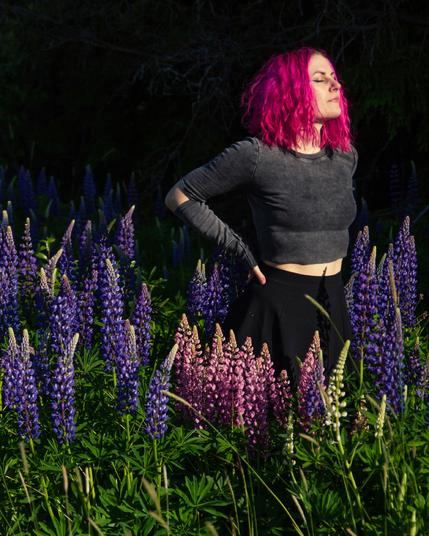 A pink haired woman enjoying sunshine surrounded by lupines