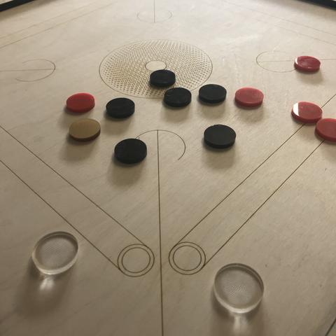 It’s a game called caroms. It looks like billiards or pool if made out of circular discs for the balls and the table and pockets are square and made of wood.