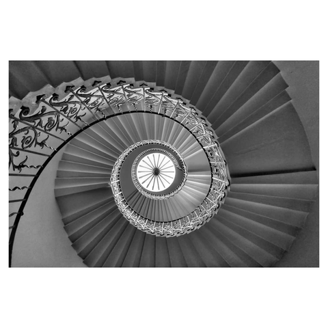 This is a black and white landscape format image looking up through a spiral staircase. A skylight sits at the centre with the stone stairs and ornate metalwork Bannister's curving from the left and spiralling to the centre of the image. Taken in the Queen's House, Greenwich, with a Sony RX100.