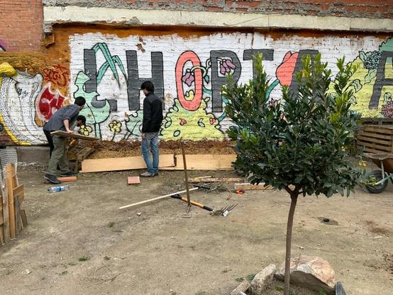 Tres persones treballant montant un bancal nou, és veu part d'un mural que possa "L'Horta...".