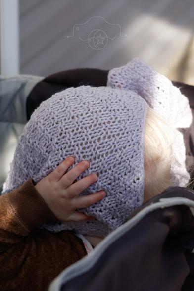 A young child plays peekaboo with a light-purple knit blanket.