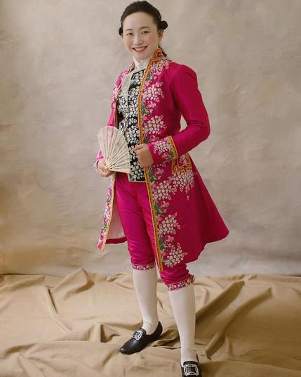 Christine wears a magenta court suit with a black waistcoat, all embroidered with lilies of the valley.
