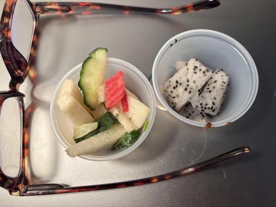 My reading glasses, framing two ramekins of food. On the left, a colorful shredded salad, on the right, a white flesh fruit with black seeds.