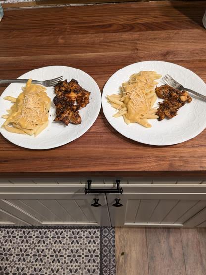 Two white plates with a serving of cajun blackened largemouth bass, and a side of penne pasta covered with pumpkin pasta sauce and a sprinkling of parmesan cheese.