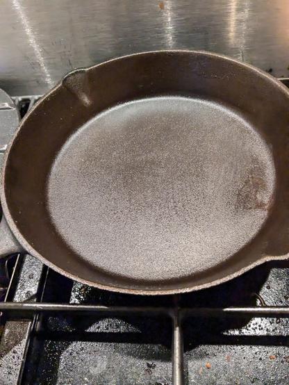 A cast iron pan sits on a stove, with a light sheen of oil on it, after having been washed and dried.