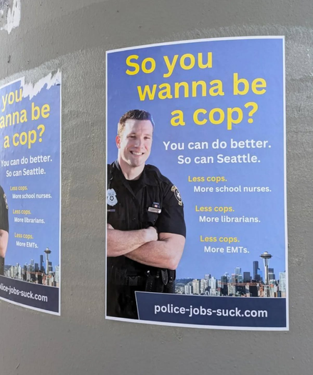 poster in Seattle with image of smiling white guy cop. Text reads: So you wanna be a cop? You can do better. So can Seattle. Less cops. More school nurses. Less cops. More librarians. Less cops. More EMTs. The bottom of the poster has the url police-jobs-suck.com.