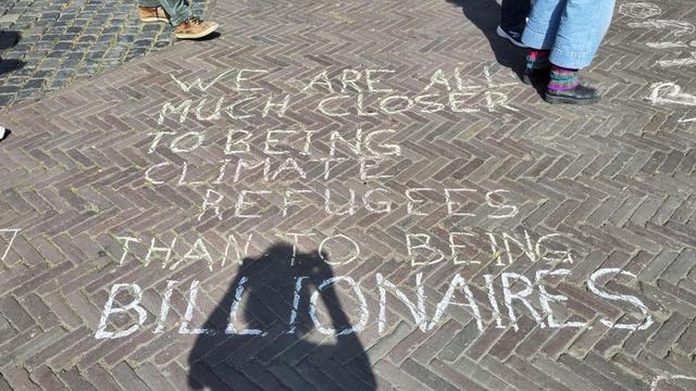 Chalk text on the street: "We are all much closer to being climate refugees than to being billionaires"