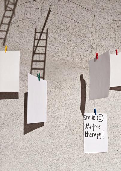 Five white papers hanging in the air and one of them has text written on it: "Smile 😊 it's free therapy!"