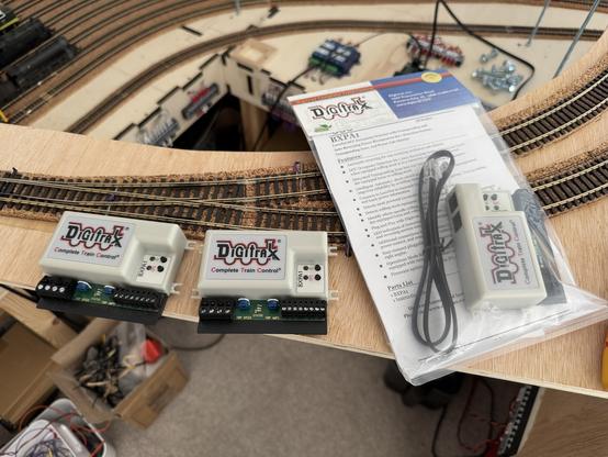 Three Digitrax BXPA1 auto reversing modules sitting on a model railway baseboards. One, delivered this morning, is in the original packaging.