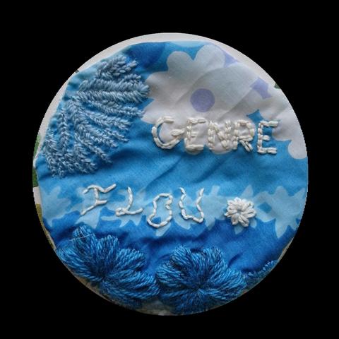 Patch brodé circulaire.
Le tissu est bleu ciel avec des motifs floraux.
En haut à gauche est brodé des épis de blés en point d'arrête bleu clair, en bas deux fleurs en passé plat bleu ciel.
Enfin, le texte brodé blanc en point de piqure en deux polices différentes lit "GENRE flou" et est accompagné d'une petite fleur blanche brodée en point de bouclette.

Le mot "flou" est tout distordu pour représenter comme un reflet flou dans l'eau