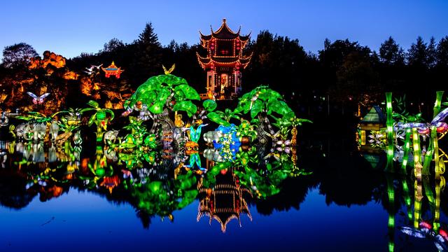 At dusk, an illuminated pagoda and multicoloured lantern, all reflected in a symmetrical way into the water.
