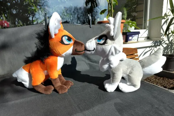 A maned wolf and a grey wolf plushie on a table with noses touching.