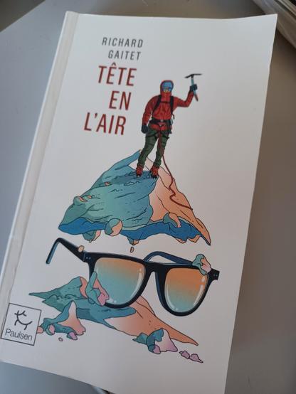 Couverture d'un livre de poche dont l'auteur est Richard Gîtes, intitulé Tête en l'air. Le dessin représente un alpiniste en haut d'une montagne levant son piolet en signe de victoire. Une paire de lunette est aussi sur le plan de la montagne (l'auteur se qualifie de binoclard)