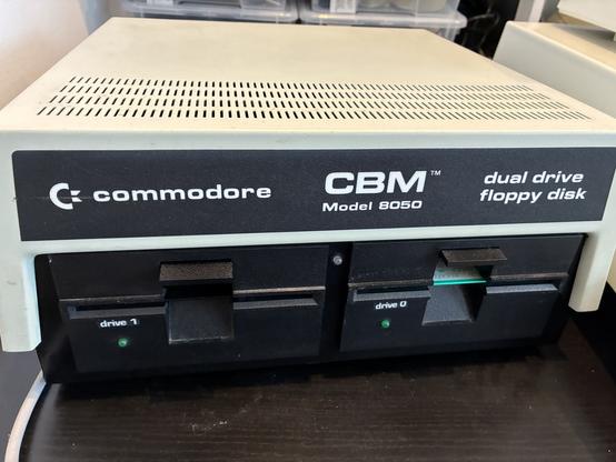 A beige and black square slab of steel case housing two full height 5.25" disk drives. A large silver Commodore and CBM logo, text says "Model 8050 dual drive floppy disk"