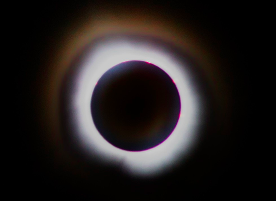 the moon sits in front of the sun. a massive halo of white light and a lighter ring of light around that can be seen against a backdrop of total black. looks like a Black Hole Sun