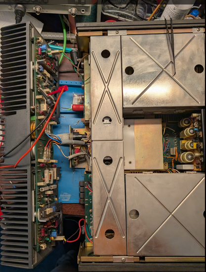 A dissambled Revox receiver sits on a very messy bench. The back part is separated from the rest of the device. Two probe leads are clipped to a resistor on the amplifier board.