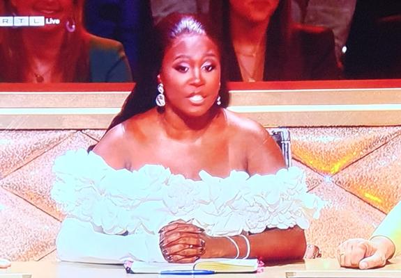 Motsi Mabuse trägt ein schulterfreies Kleid mit reichlicher weißer Blumenapplikation.