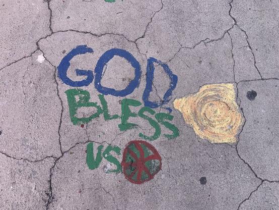 Writing within cracks on sidewalk “God” in blue, “Bless us” in green.