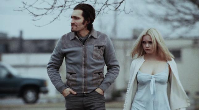 A man and a lightly clad woman walking in what looks like cold weather.