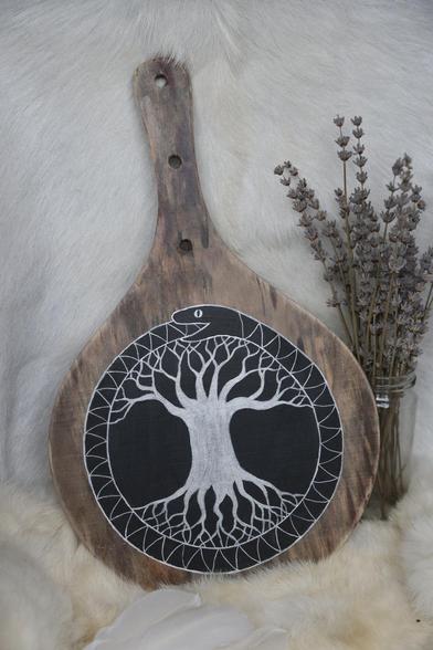 A ping pong paddle painted in silver on black with a tree of life encircled by a snake biting its own tail.