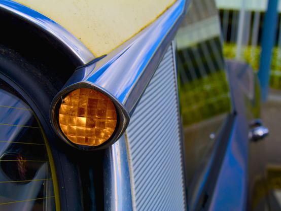 La photo représente un plan rapproché sur un phare de voiture. la cadre ne permet pas d'identifier clairement le véhicule mais son design évoque les années 50-60 et donne et effet abstrait.