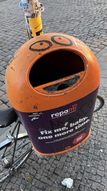 Orange garbage can with painted eyes and wide open mouth (garbage hole)