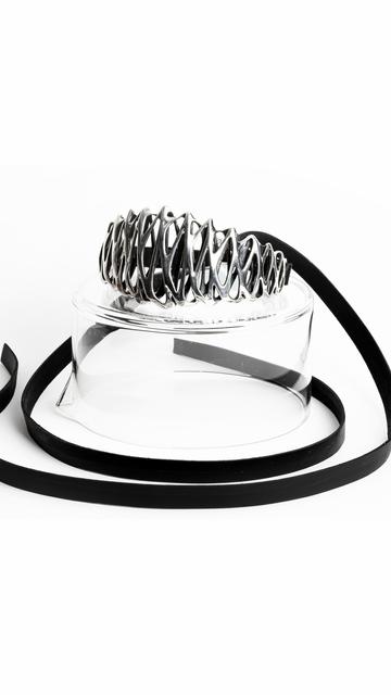 A chunky solid sterling silver necklace with adjustable black leather straps sits on a lab-glass beaker. The outer surfaces of the intricate silver grille are polished to a mirror finish. The recessed areas are contrast oxidized to a matte black finish, adding extra depth and dimension to the piece.
