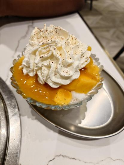 A cup of mango bingsu with whipped cream on top