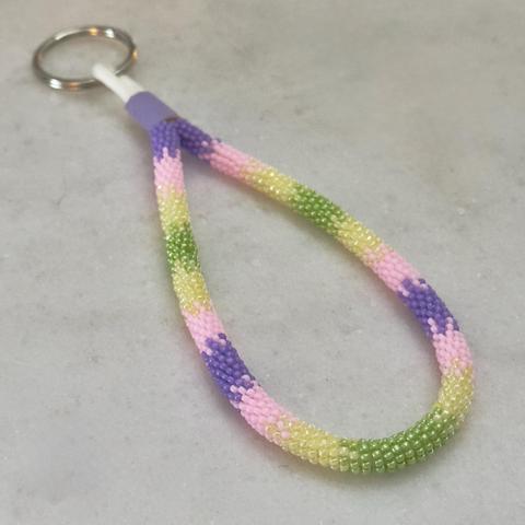 A bead wrapped wristlet keychain in purple, light pink, buttery yellow, and green