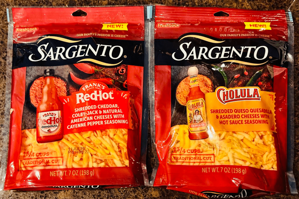 Two bags of Sargento shredded cheese, one with Frank’s RedHot flavoring and another with Cholula flavoring.
