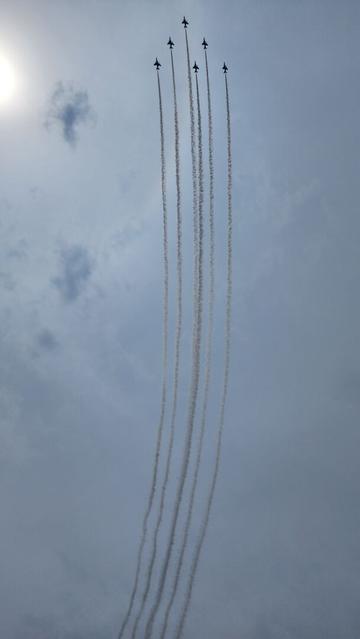Six jet planes fly in tight formation through a cloudy sky, leaving long trails of white smoke behind them.