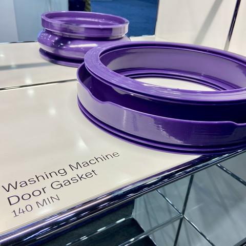A shiny, bright purple washing machine door gasket on a white display shelf. There is a label saying it took 140 minutes to print. Another purple gasket, somewhat taller, is visible in the background.