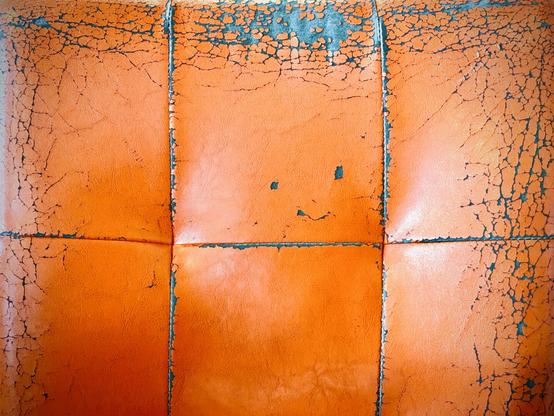 An orange vinyl seat-back is adorned with cracks all around its edges and seams, along with what look like a mouth and eyes, while raising one of its eyebrows in a seemingly judging way.