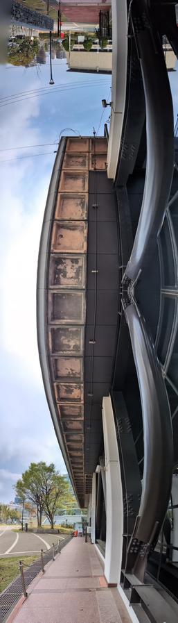 福岡県立美術館の玄関付近の縦長パノラマ。前は福岡市民ホール、後ろは福岡市民会館。右側は耐震補強の黒い柱。