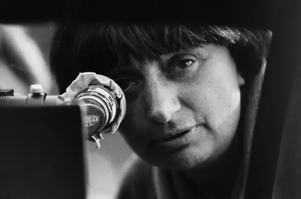 Black & white image of the artist looking through the lens of a camera, with one eye on the viewer.
Credit: Micheline Pelletier