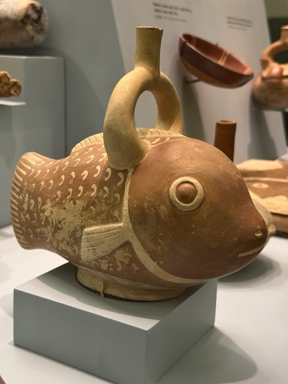 photo of the first parrotfish ceramic vessel on display at museum, quarter turn side profile: single ring spout on top, orange-brown with lighter yellow-brown spout and detailing of scales, find, facial features