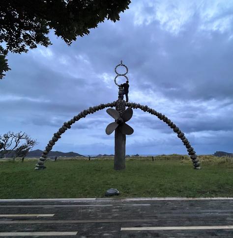 Rainbow Warrior memorial monument in Matauri Bay with a dramatic cloudy sky and a person climbing on top of it.