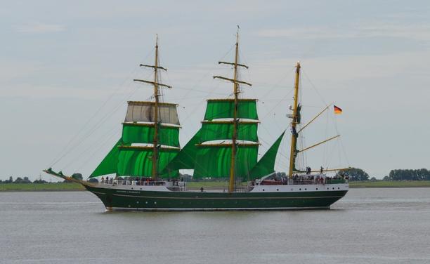 Segelschiff mit grünem Rumpf, weißen Aufbauten und grünen Segeln. Im Hintergrund das Ufer eines Flusses. 

Foto: Martin Marheinecke