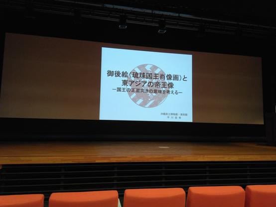 photograph of the stage and the screen with the first slide 「ugui (ryukyu kings portraits) and images of the emperors of east asia, thinking about the meaning of representing the king facing front」by… hirakawa nobuyuki ? there's no reading for his name anywhere…