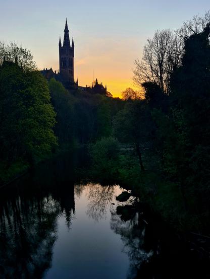 The Gothic tower of Glasgow University rising above the river Kelvin and silhouetted against the sunrise.