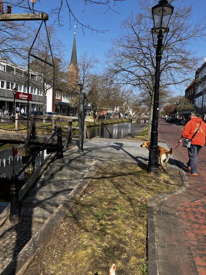 An einem der Kanäle in Papenburg . Nach links geht eine Brücke über den Kanal, rechts ist eine kaum befahrene Straße und es stehen einzelne kleine Bäume am Kanal