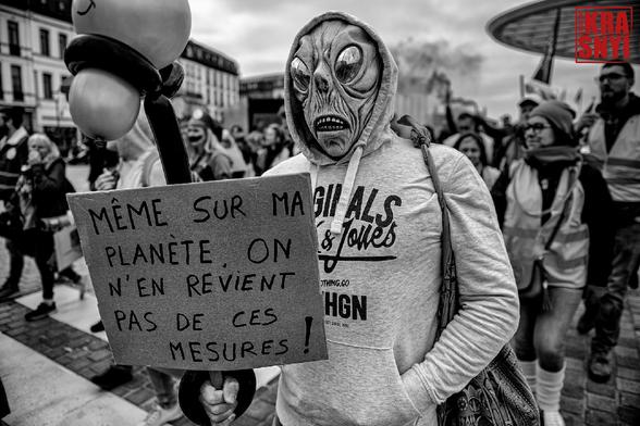 Un manifestant avec un masque d'alien et une pancarte: "MÊME SUR MA PLANÈTE ON N'EN REVIENT PAS DE CES MESURES"