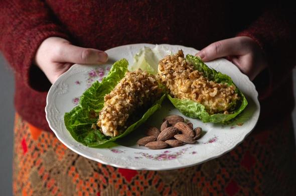 Kvinne holder en hvit tallerken med banansalat på. Bananen er skåret i to, og rullet i majones og valnøtter. Delene er så plassert på hvert sitt salatblad. Servert med salte mandler, som ligger på tallerkenen mellom bananene.