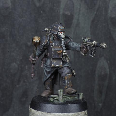 Photo of a painted miniature of a Death Korps of Krieg field engineer. They're standing up, left leg on a rotten piece of wood. They're pointing their pistol straight in front of them with their left arm. They have a small trench club in their right hand.
Their trenchcoat is dark greenish grey, the heavy armour is mate black and has a lot of chipped paint revealing metal underneath. They're have a gas mask with a skull pattern on their face.