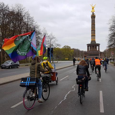 Fahrraddemo. Fahrradfahrer:innen vor der Siegessäule mit Pride-Flag.
